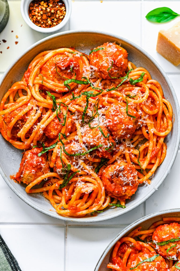 An overhead shot of a white plate of chicken meatballs tossed with sauce and noodles on a white background