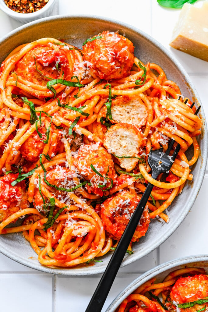 An overhead shot of a white plate with chicken meatballs tossed in sauce and noodles with a fork on the plate with spaghetti twisted on it