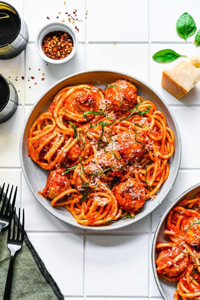 An overhead shot of a white plate of chicken meatball tossed with sauce and noodles on a white background