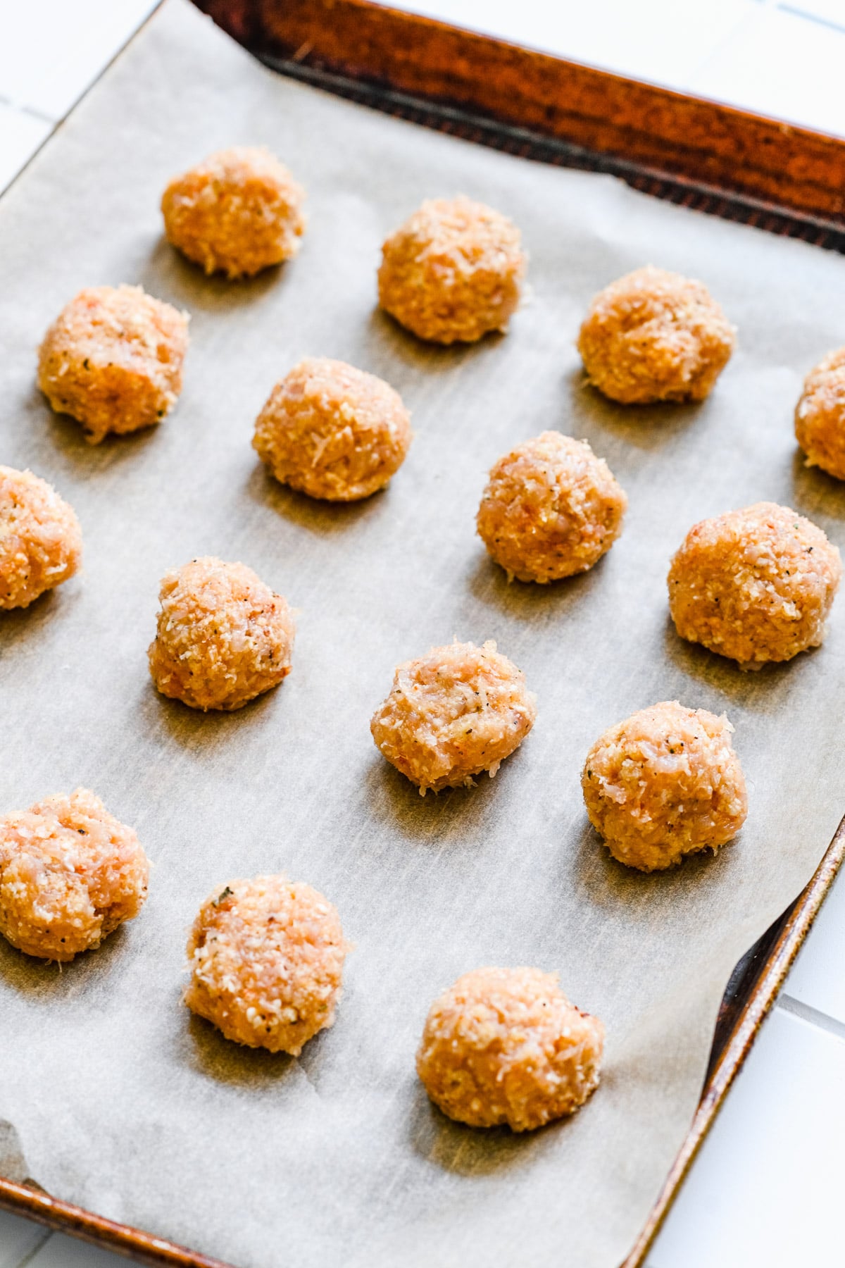 Raw chicken meatballs on a parchment paper lined baking sheet