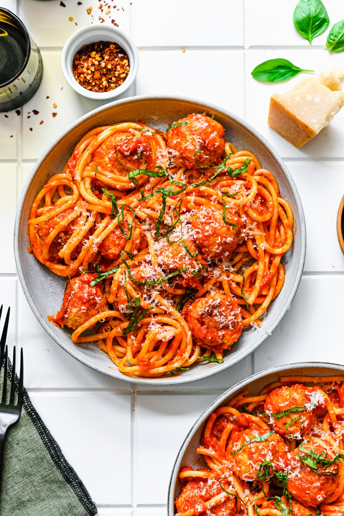 An overhead shot of a white plate of chicken meatballs tossed with sauce and noodles with another plate on the side on a white background