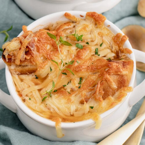 A white bowl of easy french onion soup on a blue towel with another bowl in the background