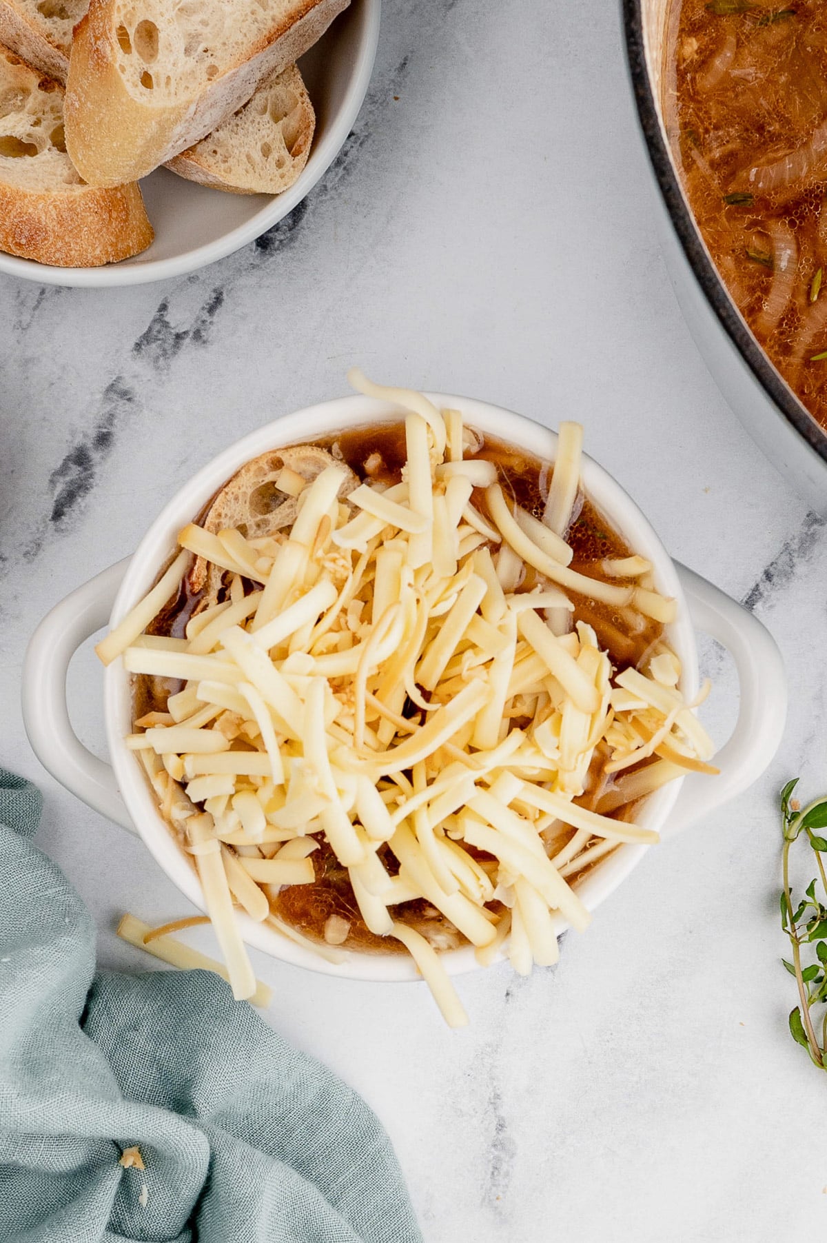 An overhead shot of a white bowl of french onion soup before melting the cheese