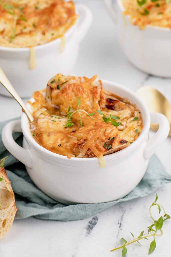 A spoon in a white bowl of best french onion soup with more bowls in the background