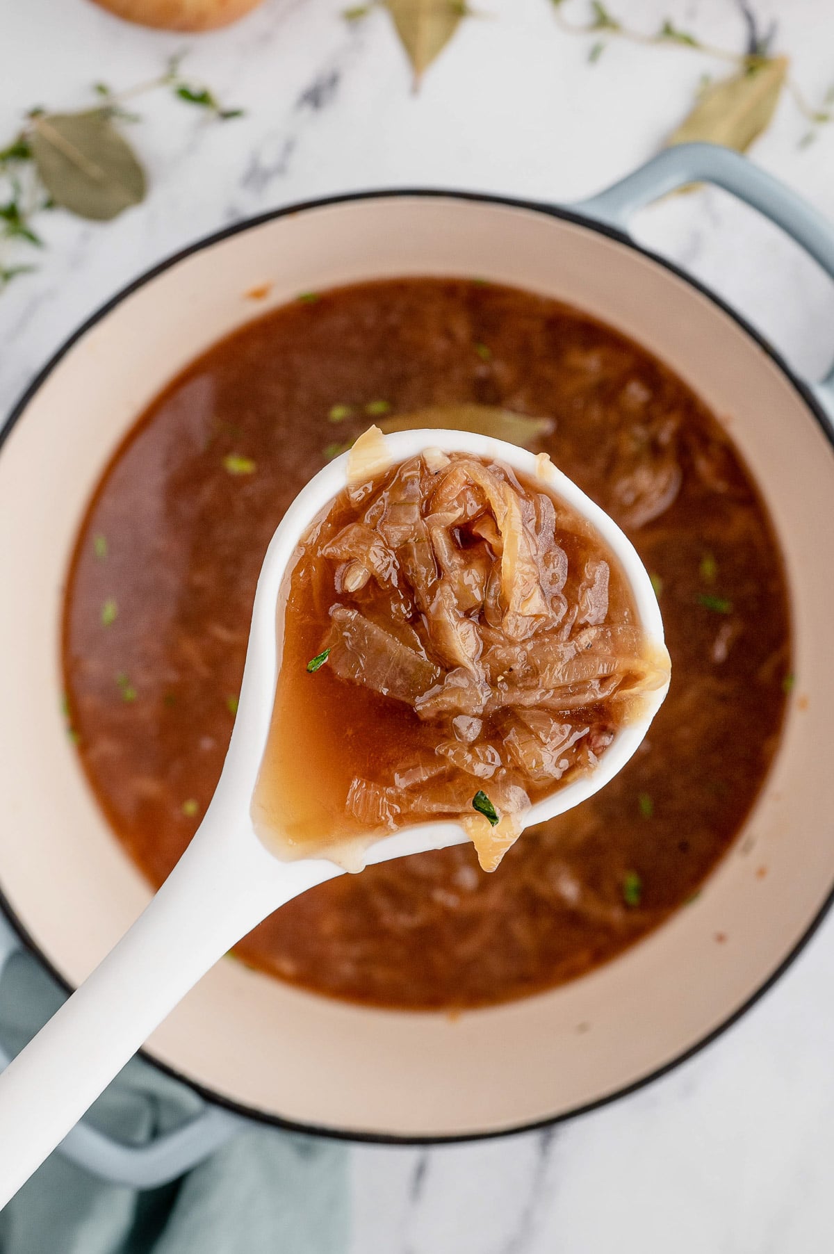 An overhead shot of a white spoon taking a scoop out of a dutch oven of french onion soup