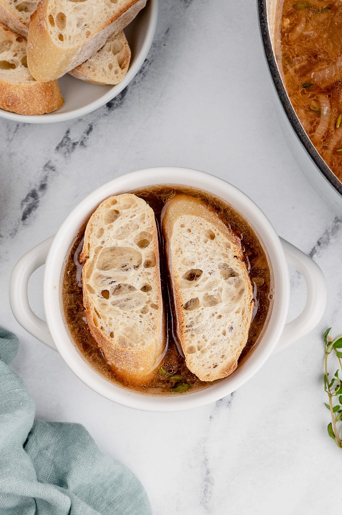 An overhead shot of a white bowl of french onion soup with toasted baguettes on top before adding cheese