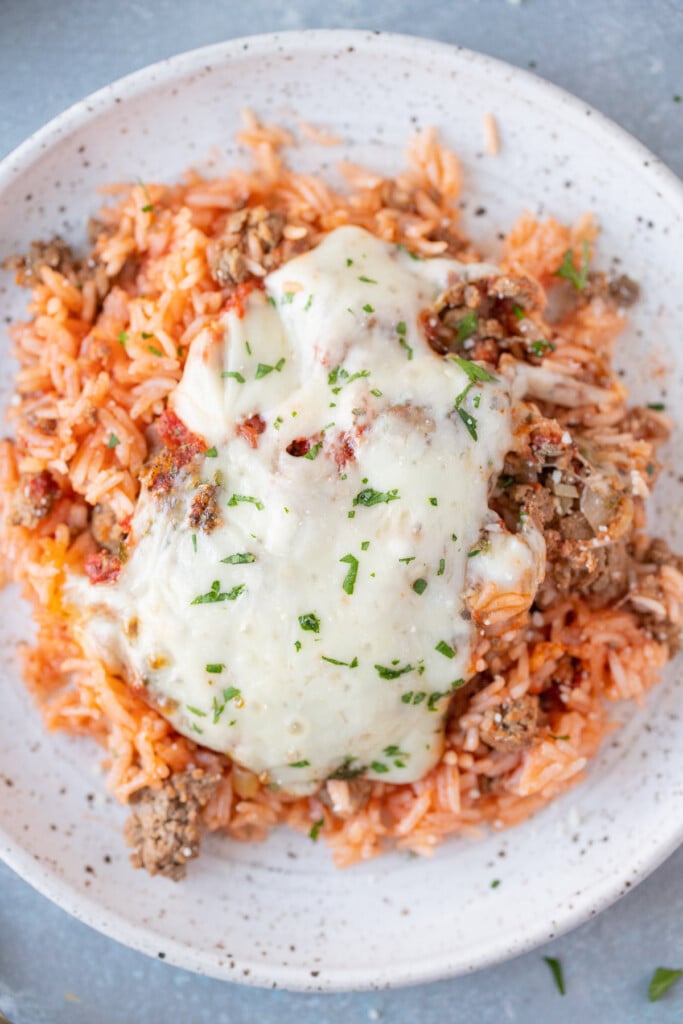 A close up of a large helping of hamburger casserole on a white plate on a grey background