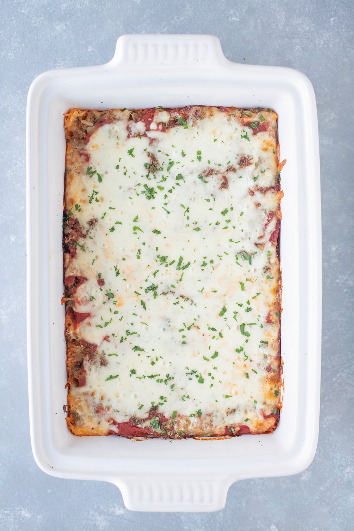 An overhead shot of hamburger casserole in a white baking dish on a grey background