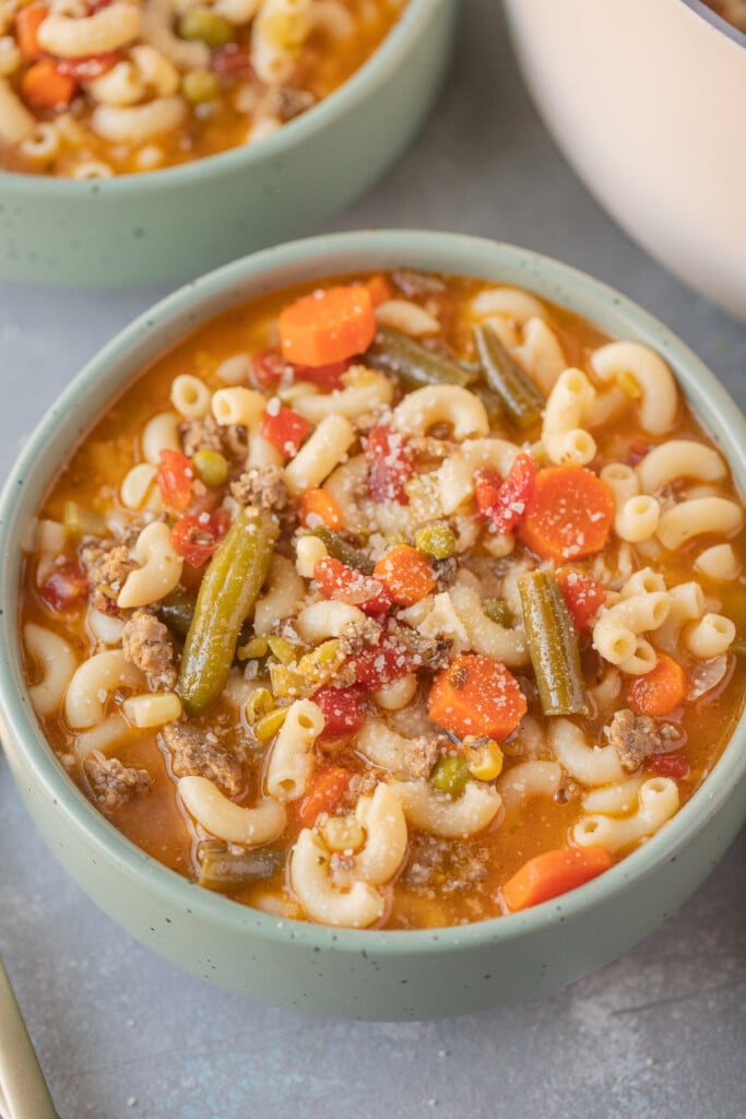 A bowl of hamburger vegetable soup on a grey background with another bowl in the background
