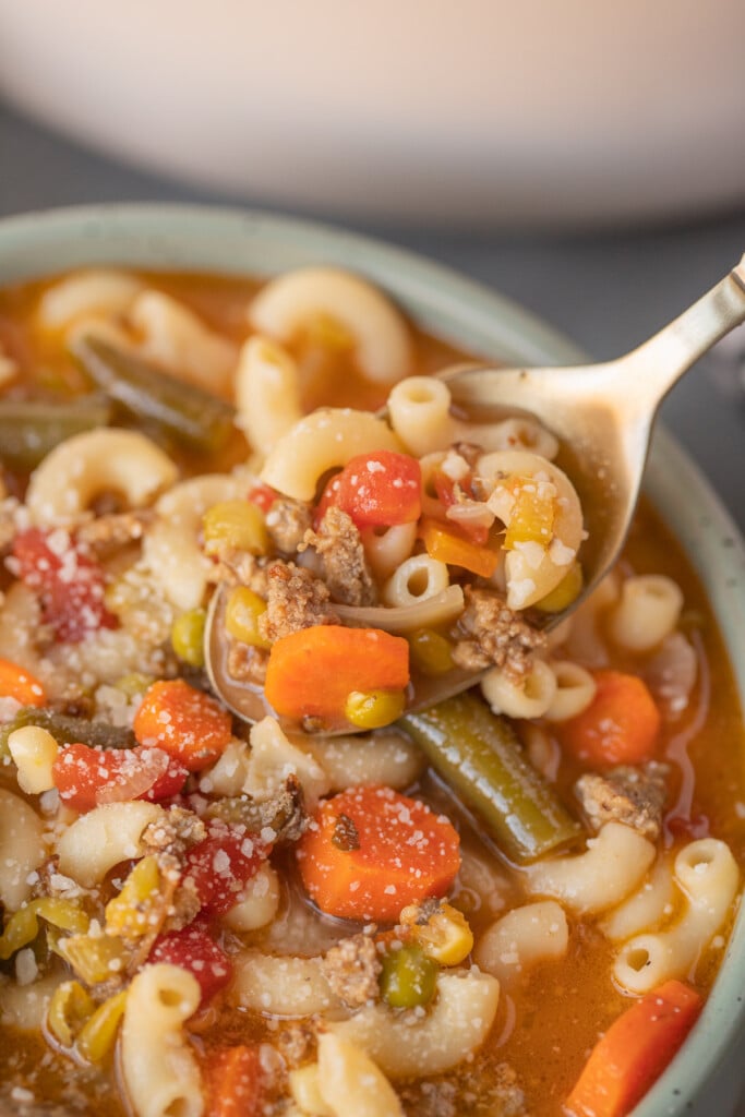 A spoon taking a bite out of a bowl of hamburger vegetable soup