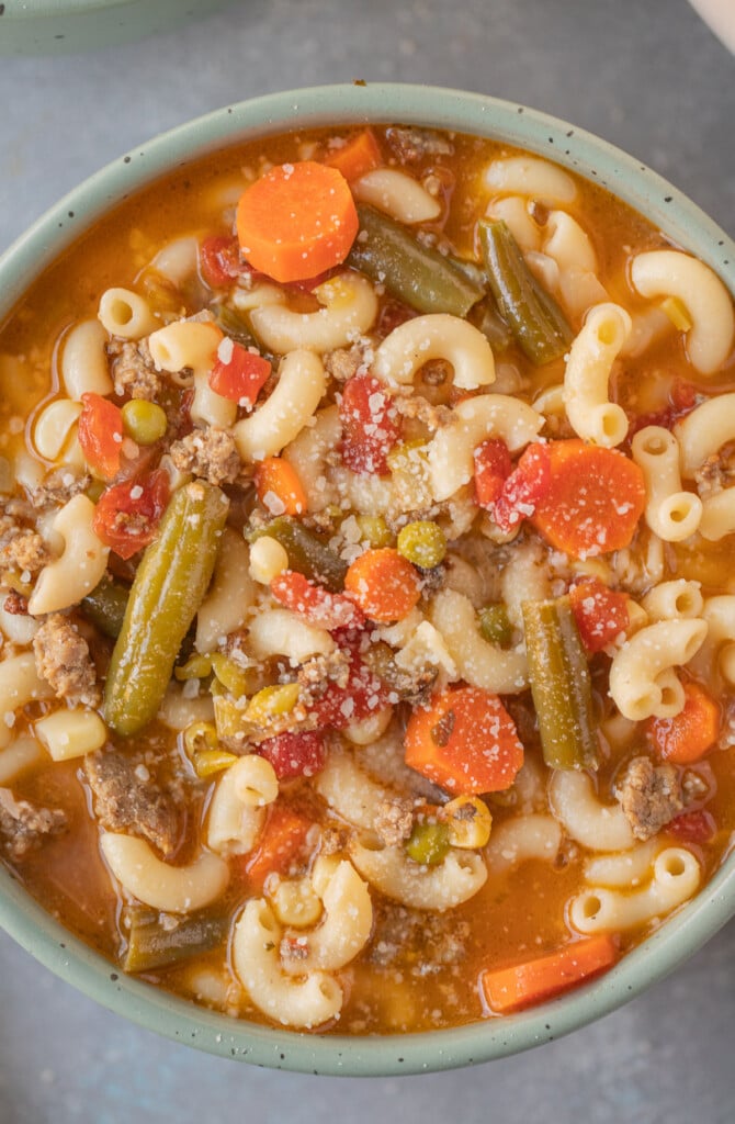 An overhead shot of a bowl of hamburger vegetable soup on a grey background
