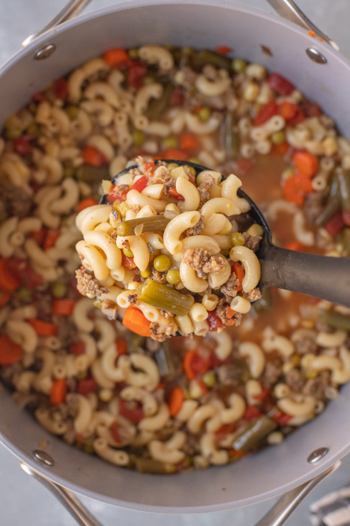 A ladle taking a large scoop of hamburger vegetable soup out of a pot