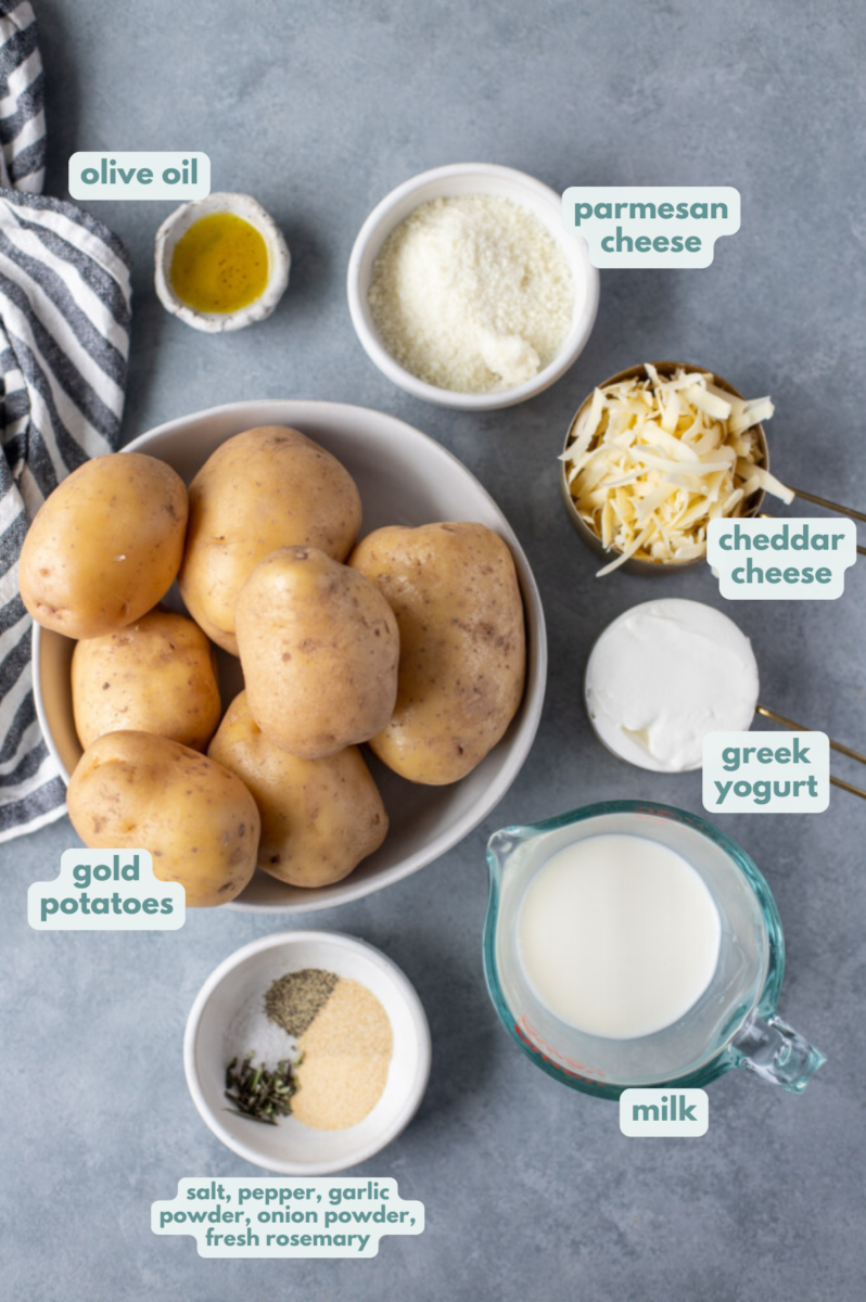 Ingredients for healthy mashed potatoes in white bowls: gold potatoes, olive oil, parmesan cheese, cheddar cheese, greek yogurt, milk, salt, pepper, garlic powder, onion powder, fresh rosemary