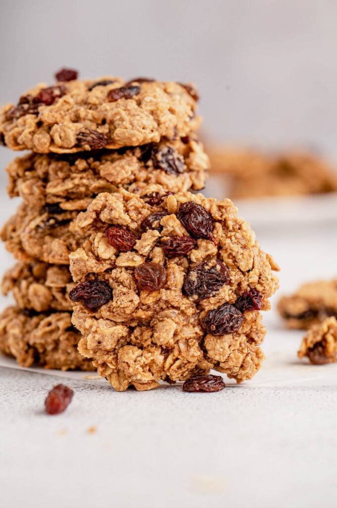 A oatmeal raisin cookie leaning on a stack of healthy oatmeal raisin cookies on a grey background