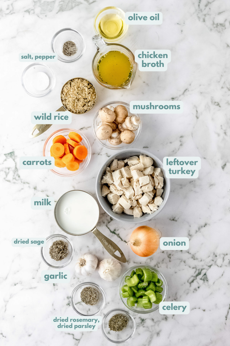 Ingredients for turkey wild rice soup in white bowls: olive oil, garlic, onion, celery, carrots, mushrooms, dried parsley, dried sage, dried rosemary, pepper, cooked turkey, wild or brown rice, chicken broth, unsweetened coconut milk