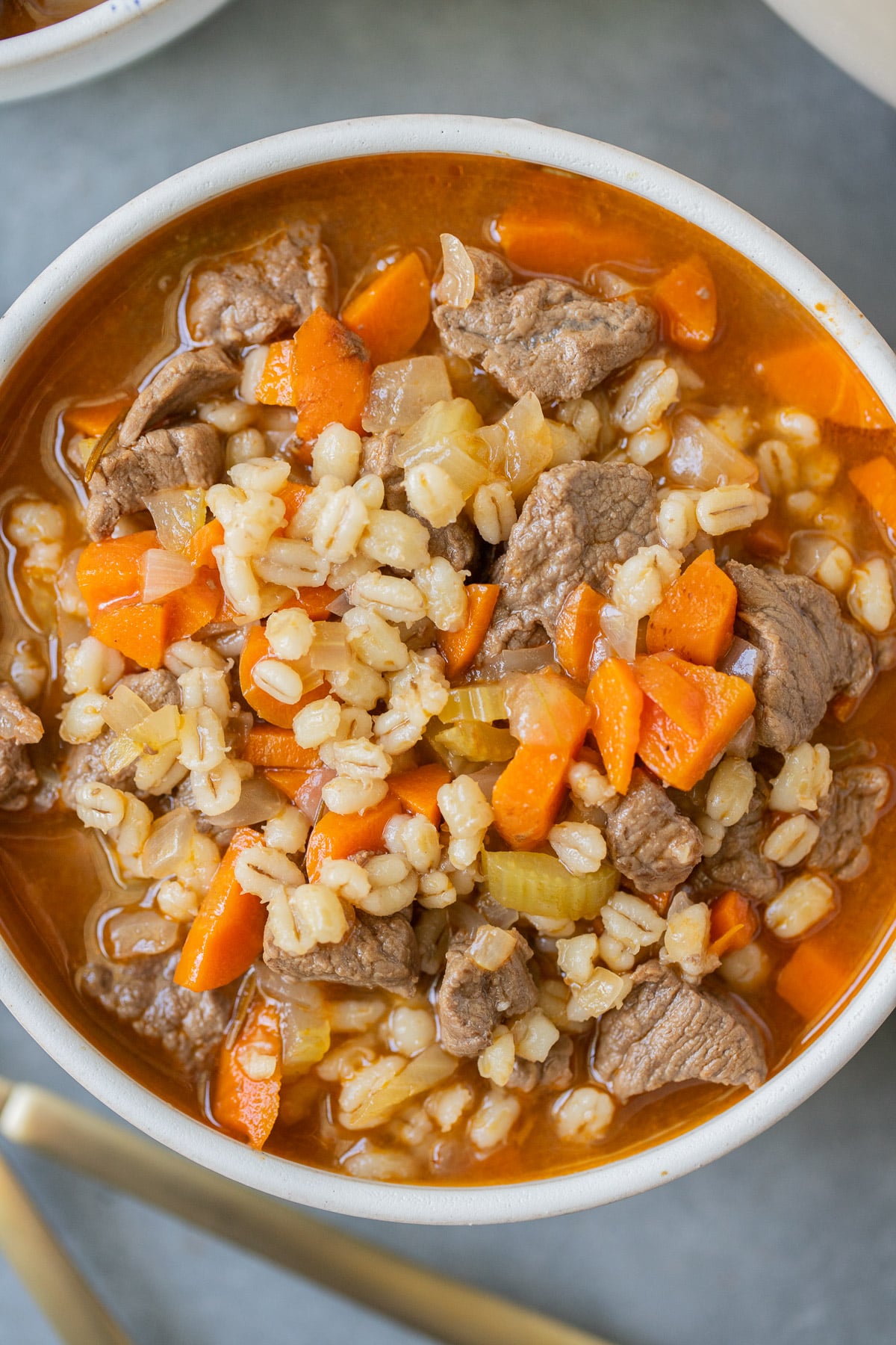 An overhead shot of a bowl of beef barley soup on a grey background