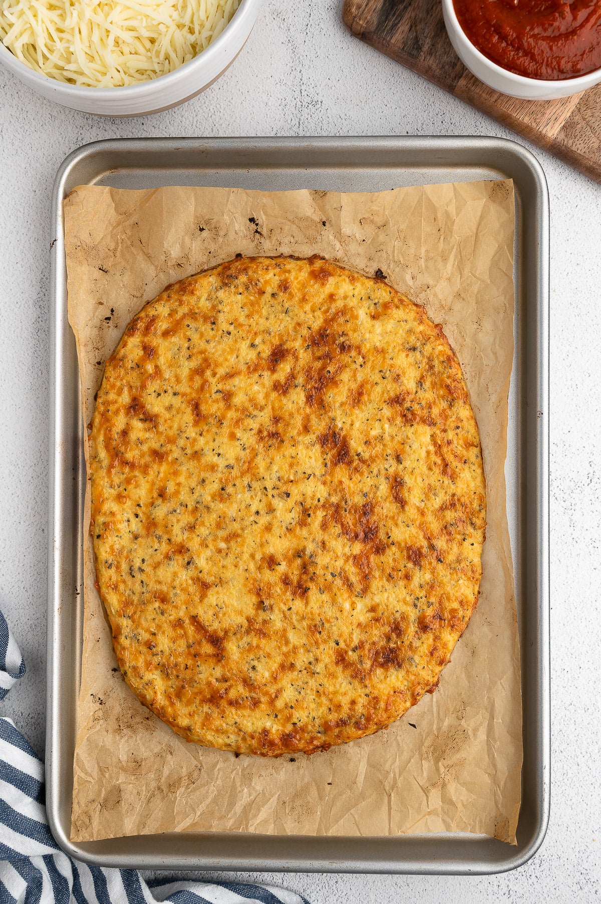 A cauliflower pizza crust on a baking sheet on a white background