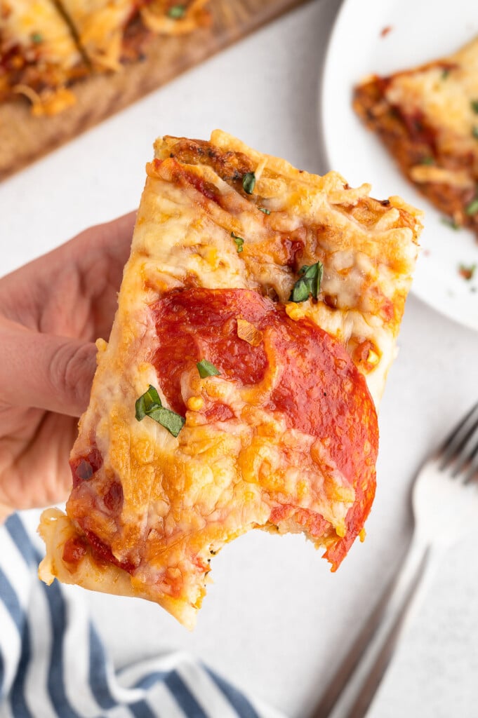 A piece of cauliflower pizza in a hand with a bite taken out of it
