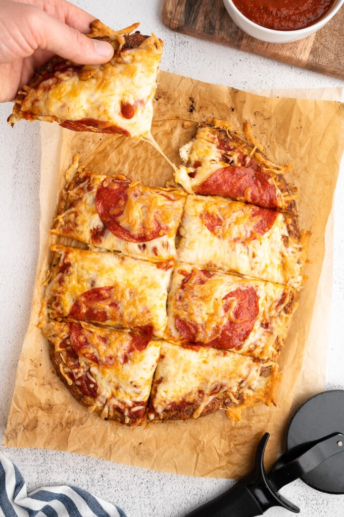 A piece of keto pizza being pulled away from the rest of the cauliflower pizza crust