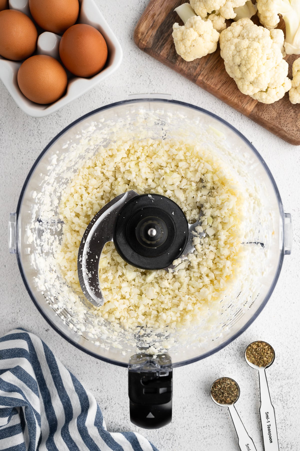 Cauliflower florets in a food processor after pulsing for keto pizza