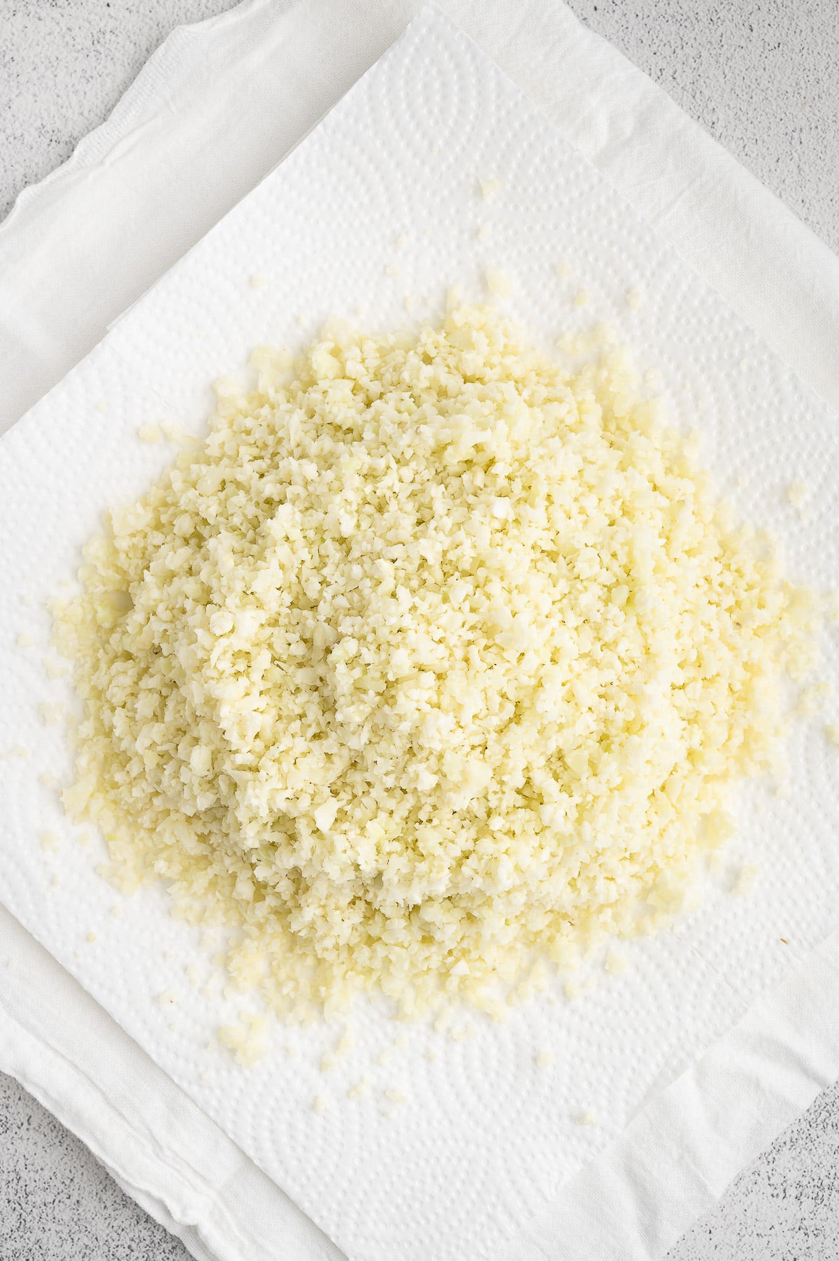 Riced cauliflower on a stack of paper towels before squeezing for keto pizza