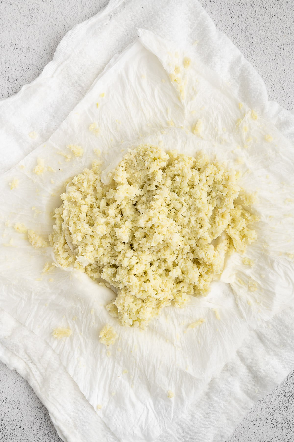 Riced cauliflower on a stack of paper towels after squeezing for keto pizza