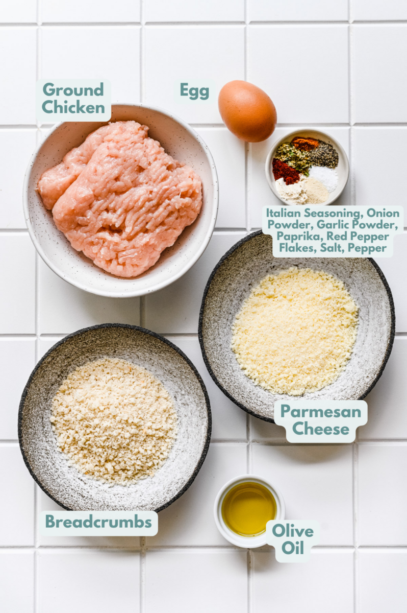 Ingredients for baked chicken meatball recipe in white bowls: ground chicken, egg, panko breadcrumbs, parmesan cheese, olive oil, spices