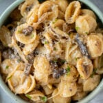 An overhead shot of a blue bowl of french onion pasta on a grey background