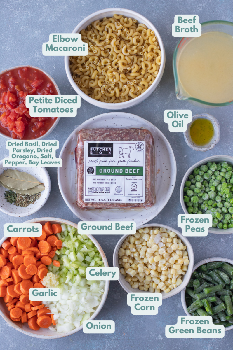 Ingredients for ground beef vegetable soup in white bowls: olive oil, ground beef, garlic, onions, celery, carrots, beef broth, petite diced tomatoes, bay leaves, dried parsley, dried basil, dried oregano, salt, pepper, frozen corn, frozen peas, frozen green beans, elbow macaroni
