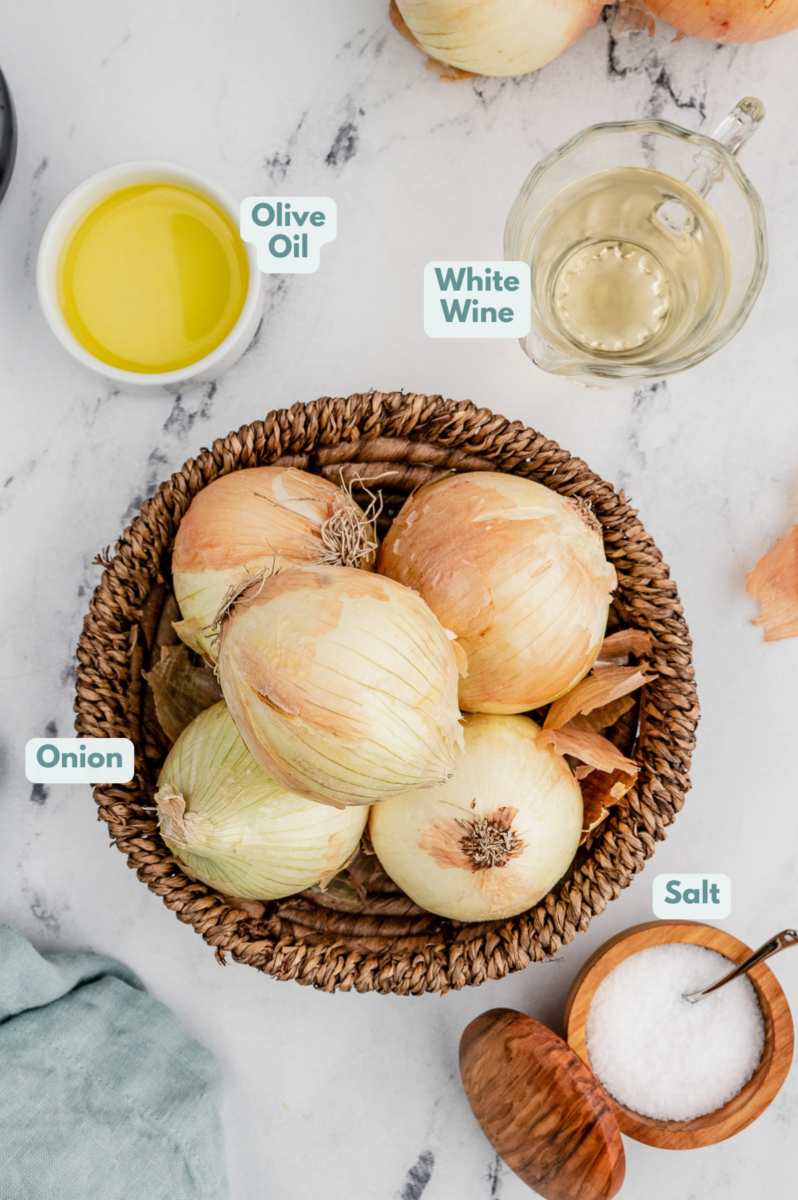 Ingredients for caramelized onions in bowls on a marble background: onions, olive oil, salt, white wine