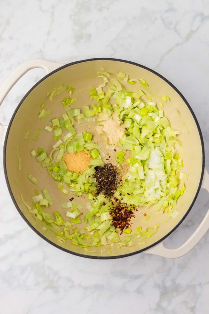 A dutch oven with garlic and leeks sautéing with spices on a grey background.