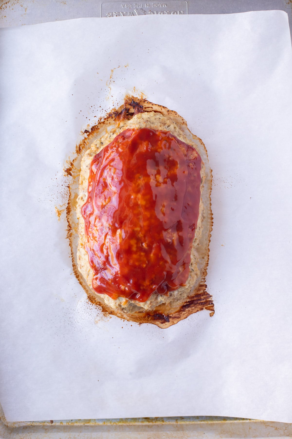 Healthy ground turkey meatloaf topped with sauce on a piece of parchment paper on a prepared baking sheet right after baking