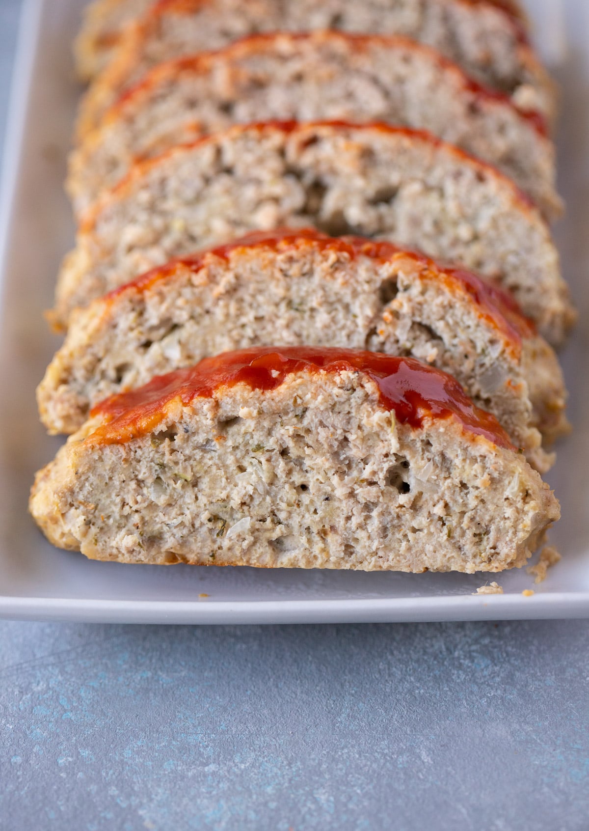 A white platter of ground turkey meatloaf on a grey background