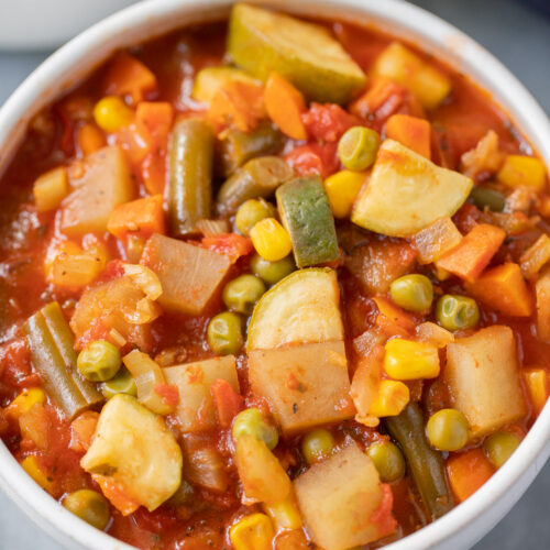 A white bowl of homemade vegetable soup on a grey background