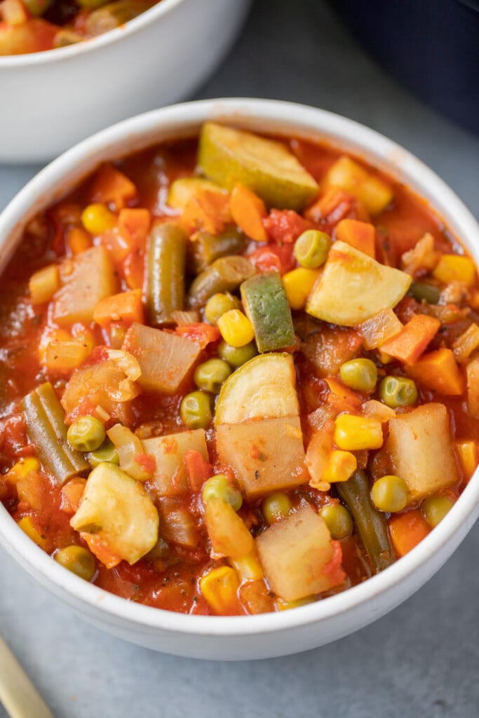 A white bowl of homemade vegetable soup on a grey background