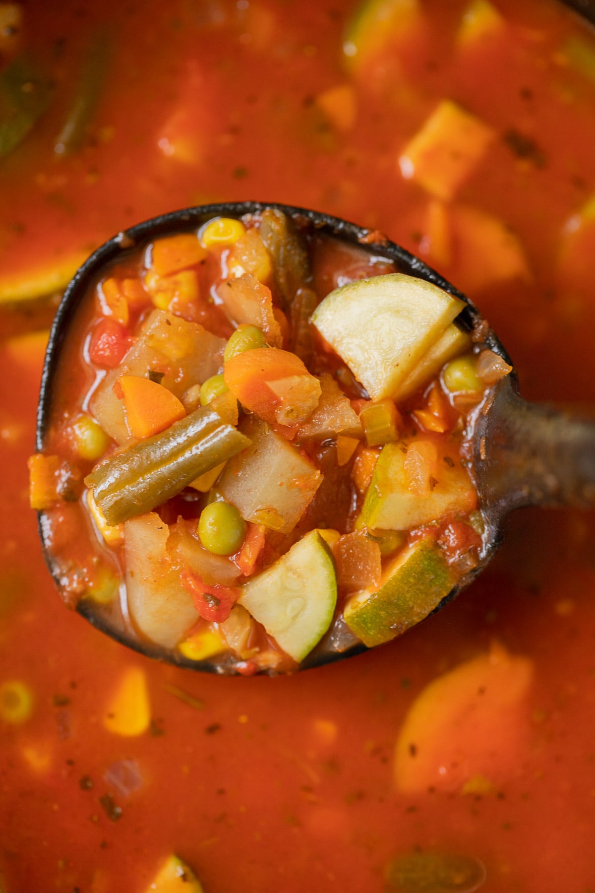 A ladle taking a large scoop of vegetable soup out of a pot