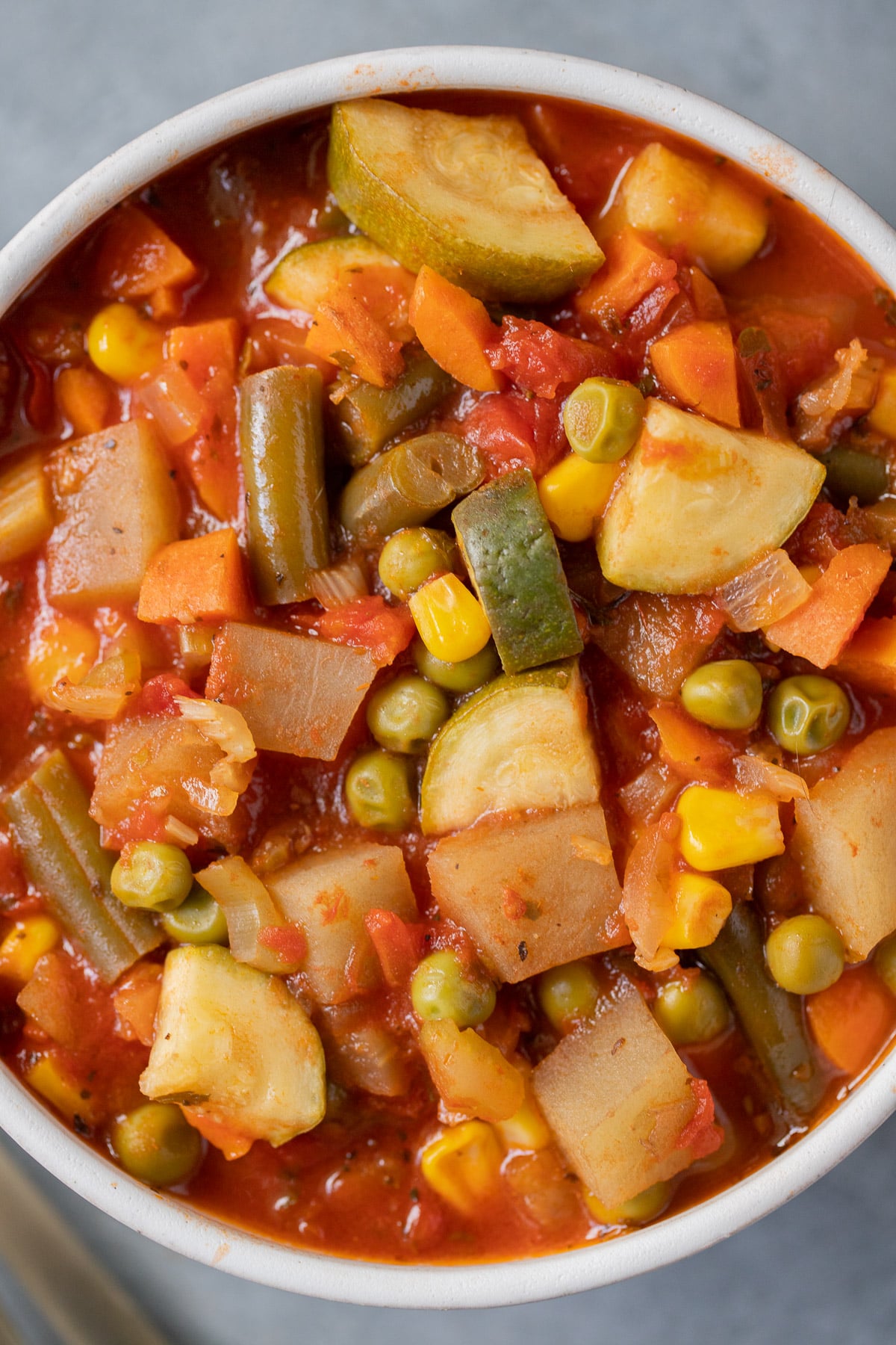 A close up of a white bowl of homemade vegetable soup on a grey background