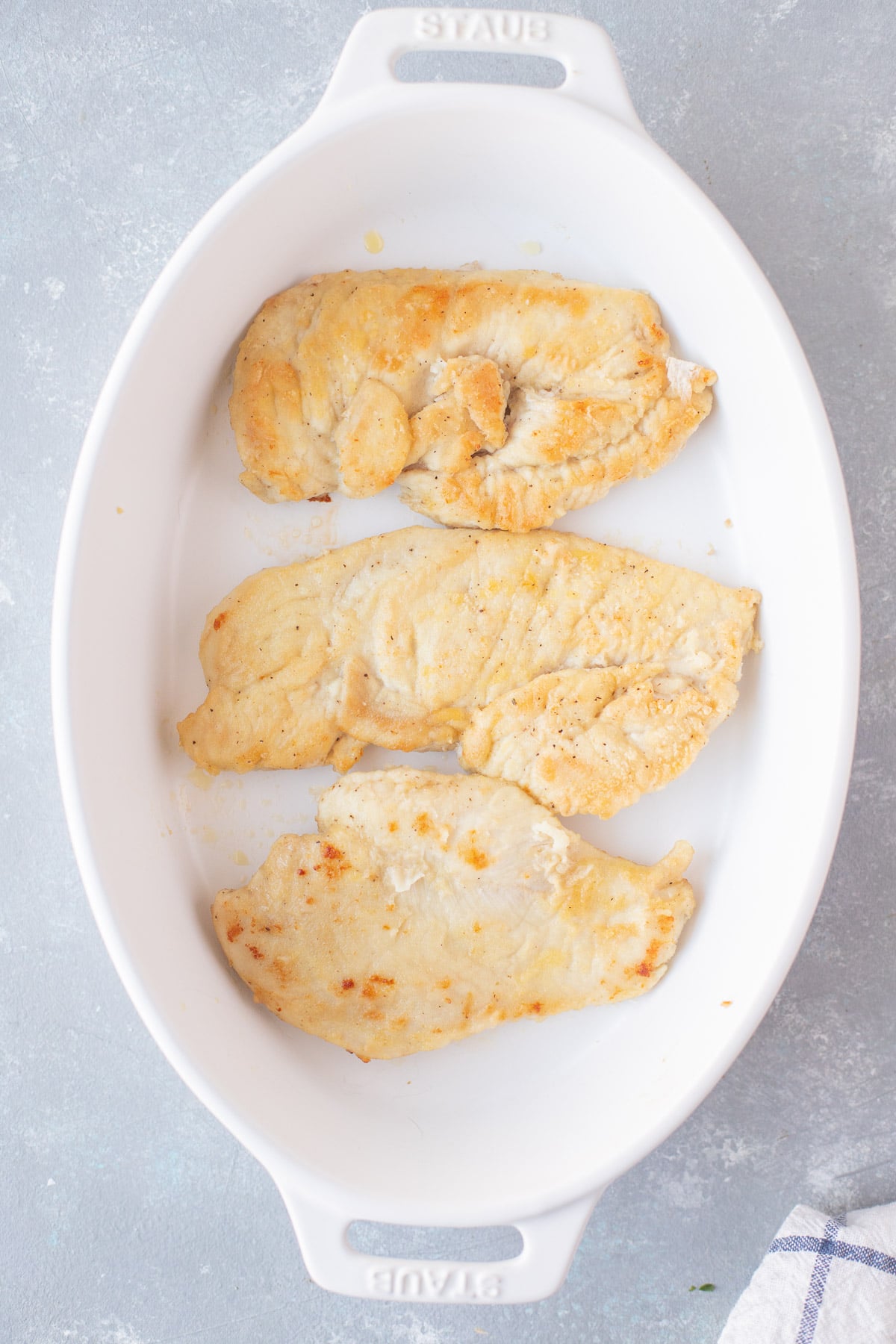 An overhead shot of chicken breast in a white baking dish for chicken marsala