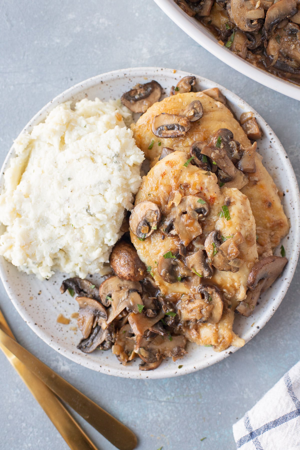 A white plate with Marsala Chicken and mashed potatoes on a grey background