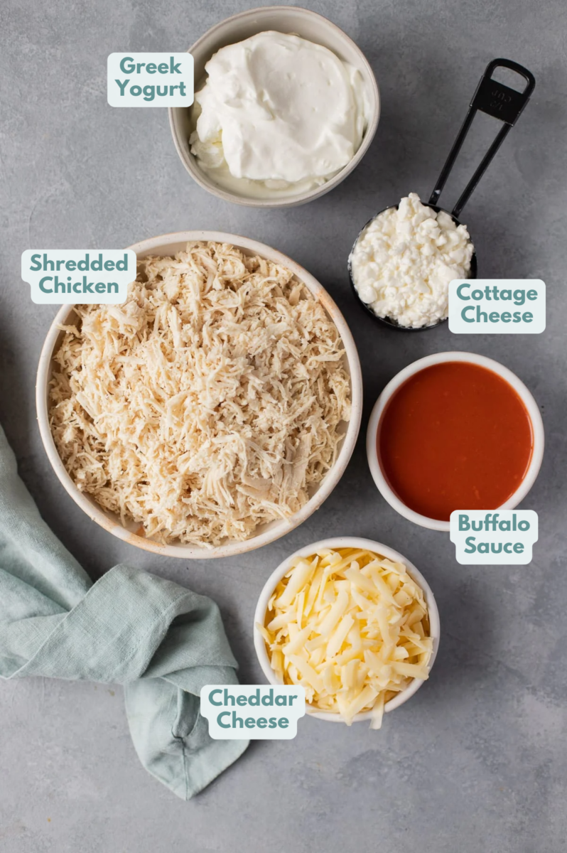 Ingredients for healthy buffalo chicken dip laid out on a blue background with a striped linen