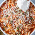 An overhead shot of lasagna soup with ricotta cheese on top on a grey background