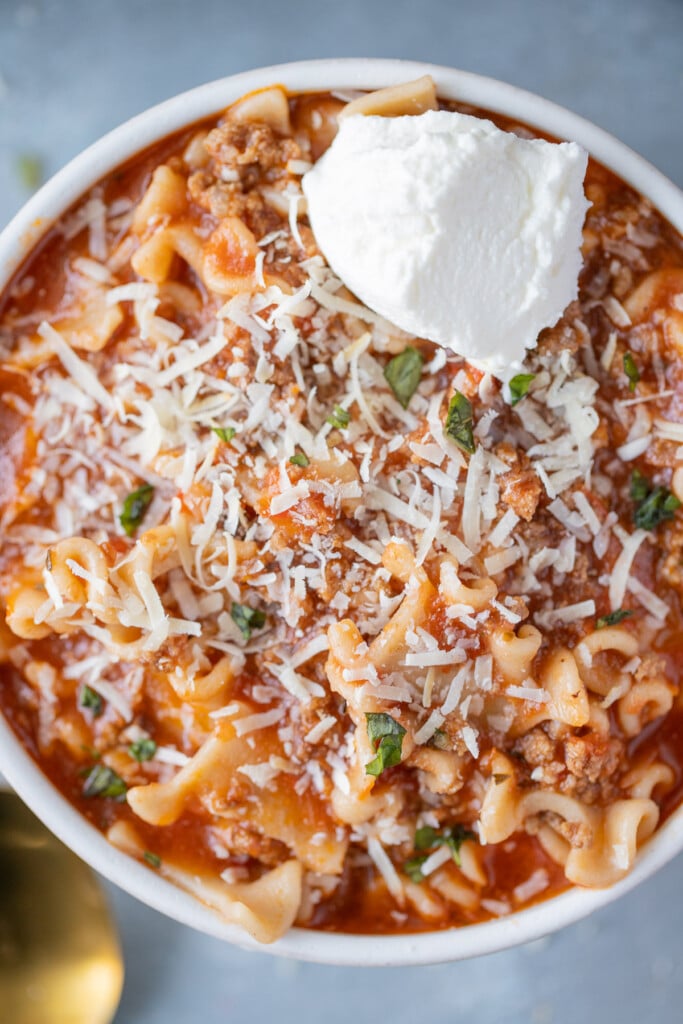 An overhead shot of lasagna soup with ricotta cheese on top on a grey background
