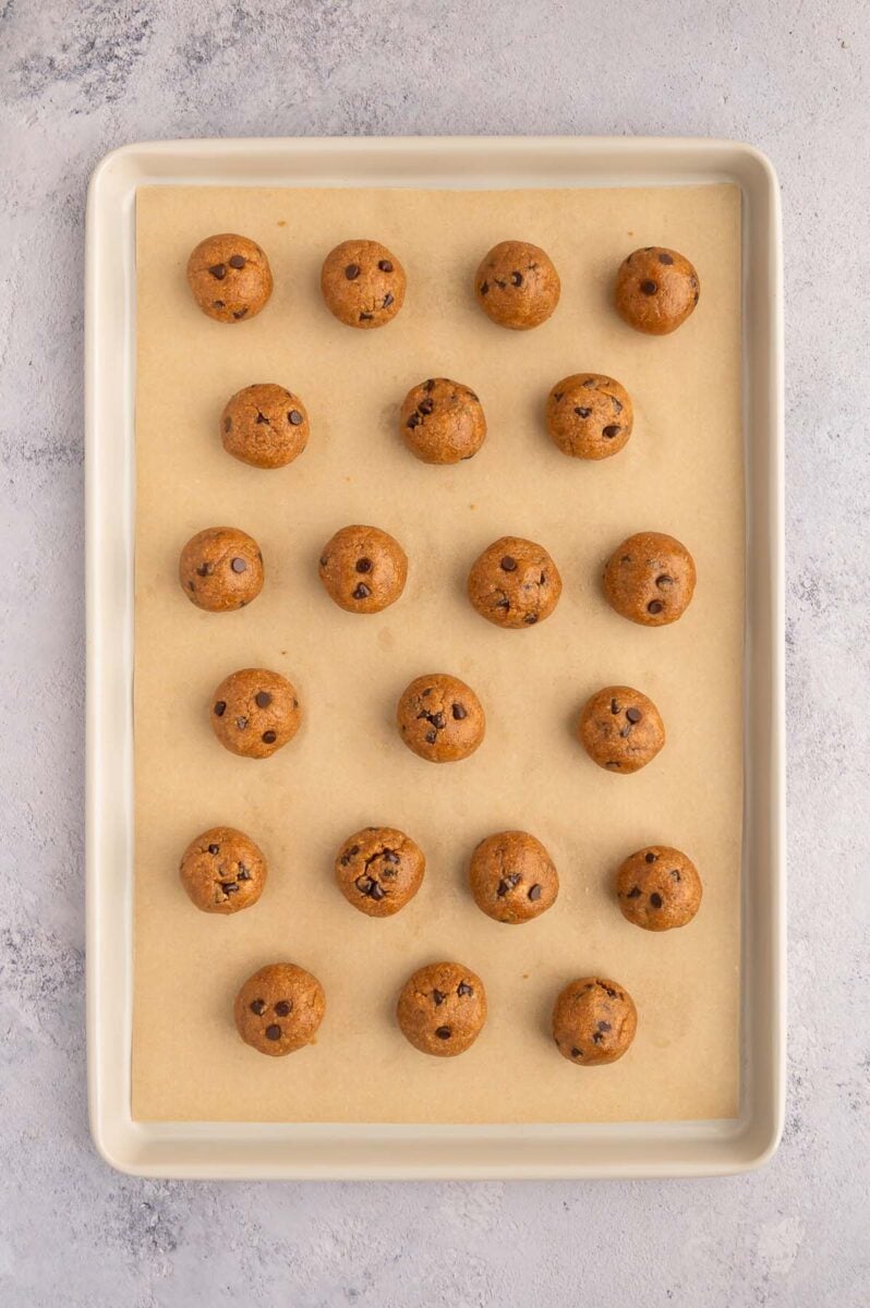 Protein cookie dough balls on a parchment lined baking sheet.