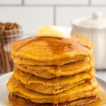 A stack of sweet potato pancakes with a pat of butter and covered in syrup on a white plate on a white background
