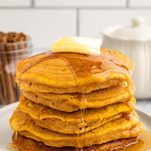 A stack of sweet potato pancakes with a pat of butter and covered in syrup on a white plate on a white background