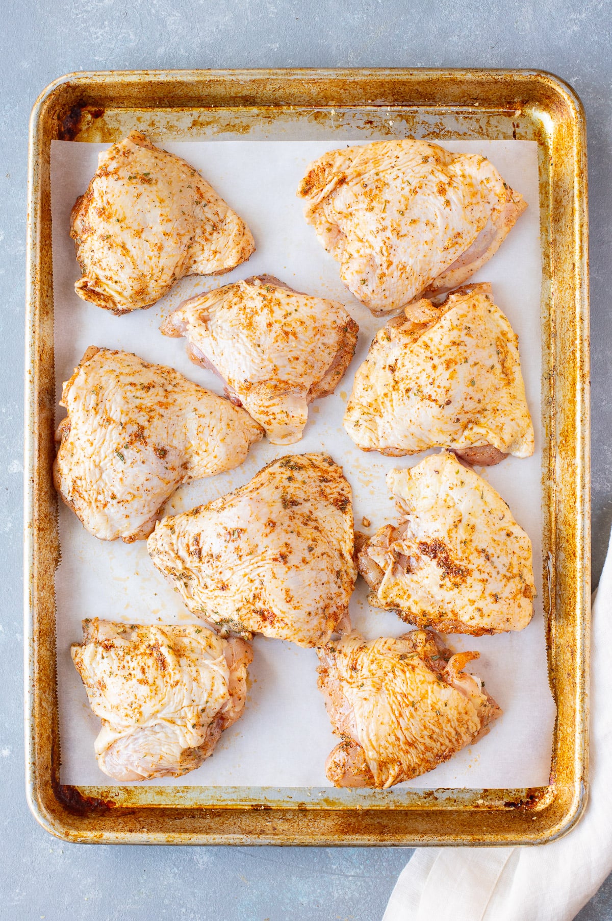 Chicken Thighs rubbed with olive oil and spices on a parchment lined baking sheet before baking