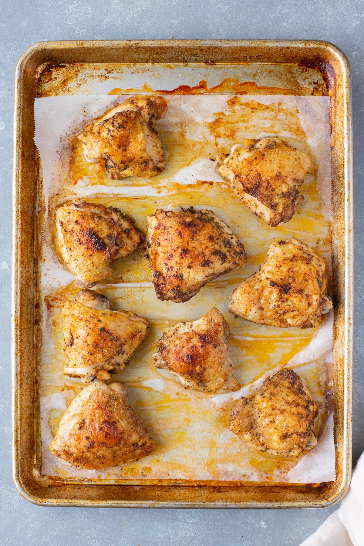 An overhead shot of baked chicken thighs on a parchment lined baking sheet