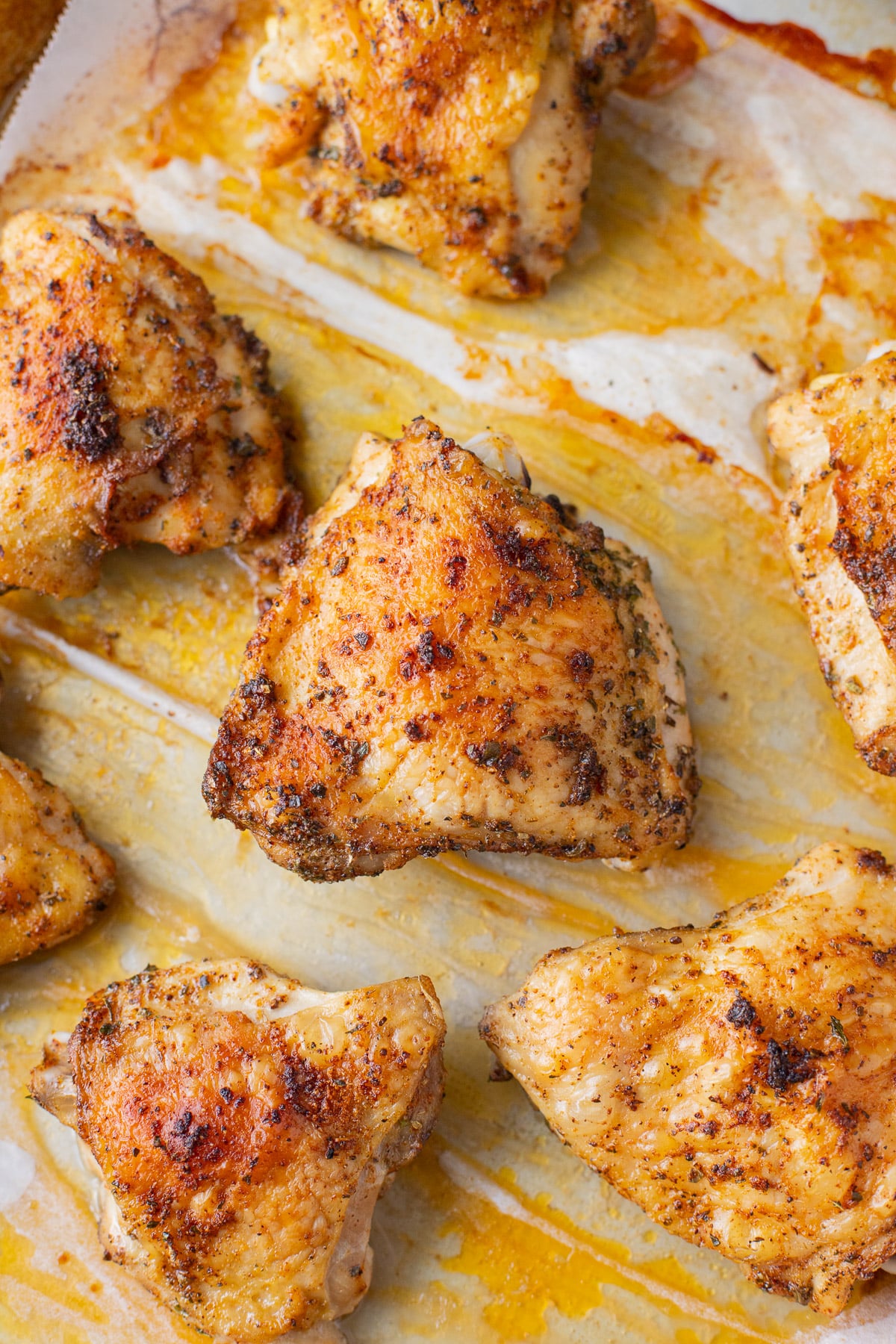 A close up shot of baked chicken thighs on a parchment lined baking sheet