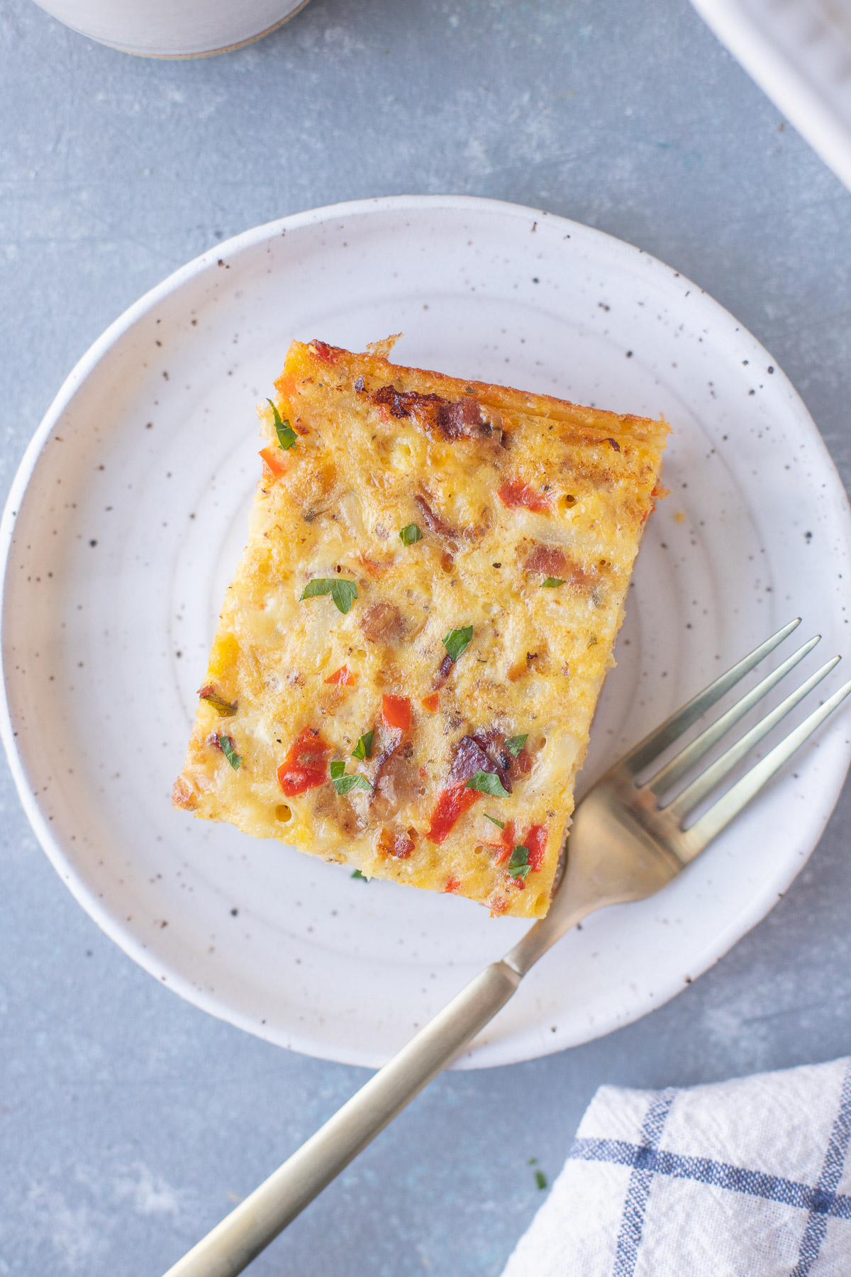 An overhead shot of a piece of bacon breakfast casserole on a white plate with a fork.