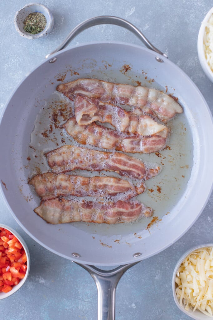 Bacon strips cooking in a pan for healthy breakfast casserole on a grey background